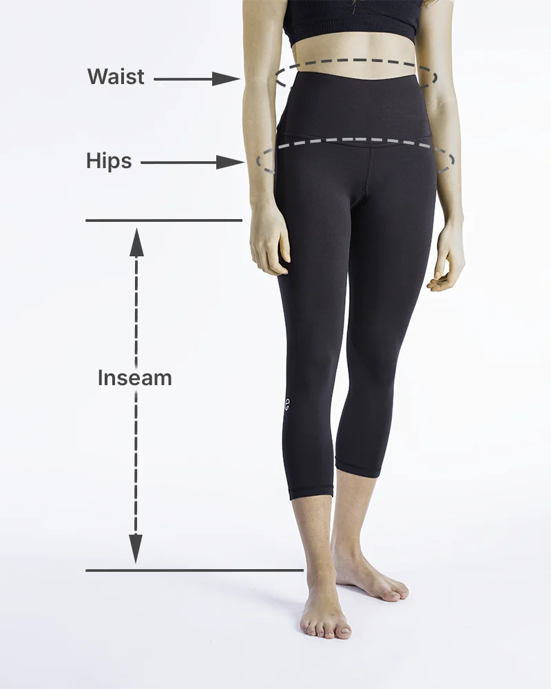 Woman wearing black high-waisted athletic leggings demonstrating how to measure waist, hips, and inseam for accurate leggings sizing. Dashed lines show where to wrap a measuring tape around the natural waist and fullest part of the hips, and a vertical line shows how to measure inseam from inner thigh to floor. Entensa size guide visual.